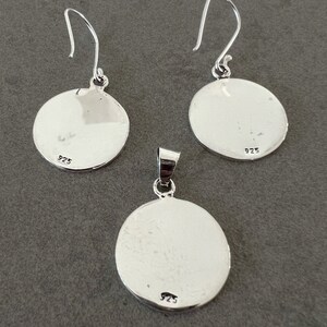 May include: A silver jewelry set featuring a pendant and a pair of earrings. Each piece has a circular design with a smooth, reflective surface. The earrings have hook closures, and all pieces are marked with "925".