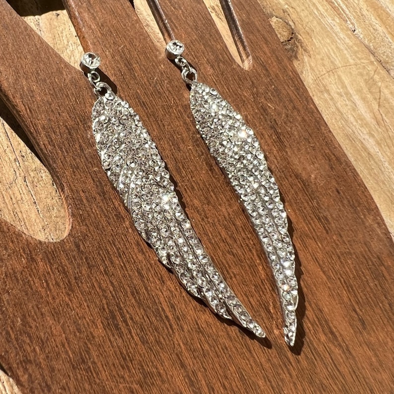May include: A pair of silver dangle earrings with crystal accents shaped like angel wings.