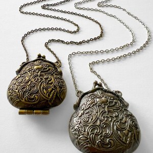 Puede incluir: Dos colgantes ornamentados, de color dorado, con bisagras, de estilo medall&oacute;n, cuelgan de una cadena plateada. Los colgantes tienen forma de monedero y presentan intrincados dise&ntilde;os florales.