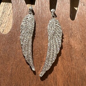 May include: A pair of silver dangle earrings with crystal wings. The wings are made of small, clear crystals that are set in a silver metal.