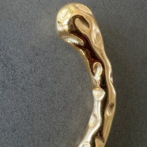 May include: A gold-colored, textured metal bracelet with a unique, organic shape.