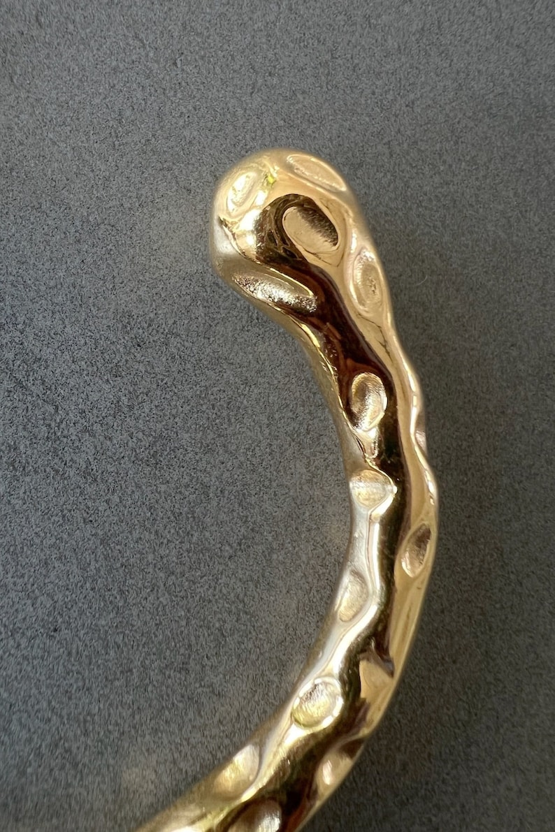 May include: A gold-colored, textured metal bracelet with a unique, organic shape.