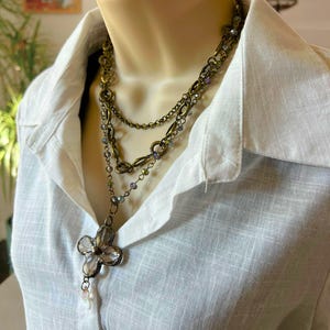 May include: A layered necklace with a large, clear crystal flower pendant. The necklace is made of multiple chains with small, iridescent beads.