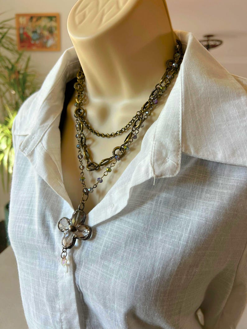May include: A layered necklace with a large, clear crystal flower pendant. The necklace is made of multiple chains with small, iridescent beads.
