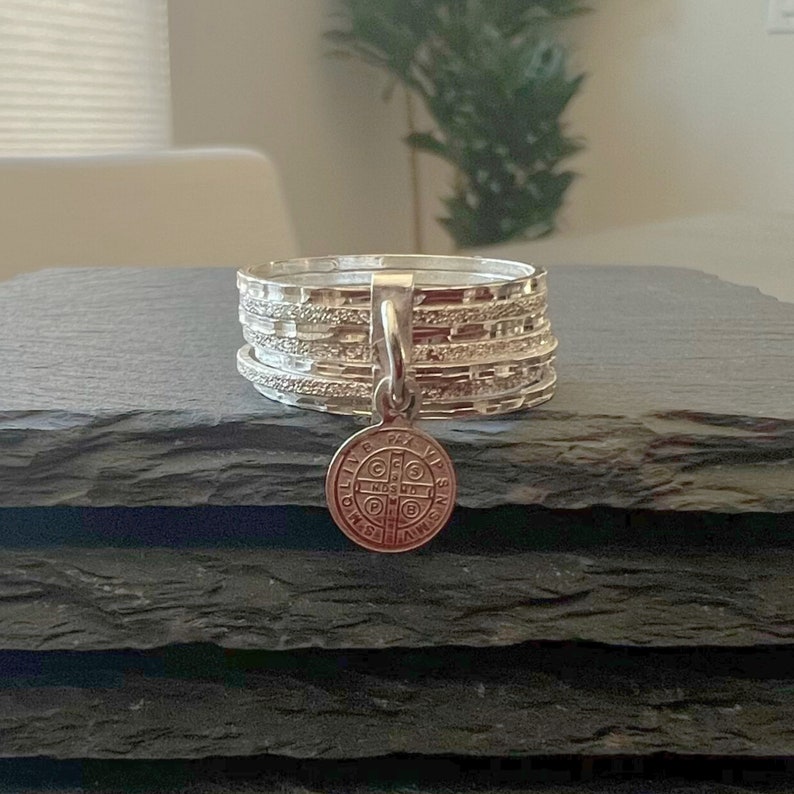 May include: A silver ring with a silver charm pendant. The charm is a round medal with a cross and the words "Ora Pro Nobis" and "Sancte Michael Archangele" around the edge.