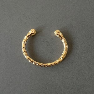 May include: A gold-toned ear cuff with a textured, hammered finish. The cuff is open and has a rounded shape.