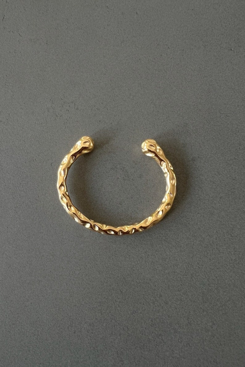 May include: A gold-toned ear cuff with a textured, hammered finish. The cuff is open and has a rounded shape.