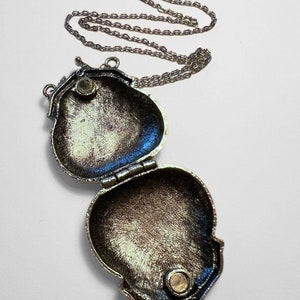 Puede incluir: Un collar de plata con un colgante en forma de coraz&oacute;n. El medall&oacute;n est&aacute; abierto, revelando un interior liso y vac&iacute;o.