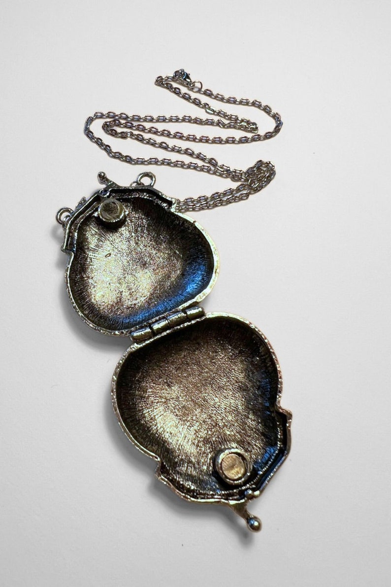 Puede incluir: Un collar de plata con un colgante en forma de coraz&oacute;n. El medall&oacute;n est&aacute; abierto, revelando un interior liso y vac&iacute;o.