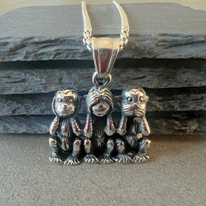 May include: Silver necklace with a pendant of three monkeys, one covering its eyes, one covering its ears, and one covering its mouth. The monkeys are in a row, facing forward.
