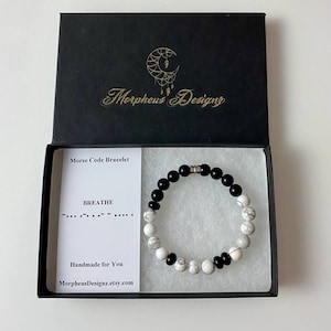 May include: A black and white beaded bracelet with a silver clasp. The bracelet is in a black box with a white card that says "Morse Code Bracelet" and "BREATHE" in Morse code. The card also says "Handmade for You" and "MorpheusDesignz.etsy.com".