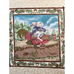 May include: A decorative fabric panel featuring a whimsical scene of a white rabbit in a blue and red striped jacket riding a rooster through a forest. The panel has a border of acorns and foliage, with a cream-colored background.