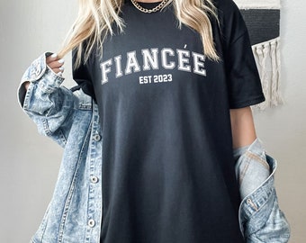 May include: Black oversized t-shirt with white text that reads "FIANCÉE EST 2023".
