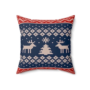 May include: A blue throw pillow with a red border features a white knitted pattern of reindeer and a Christmas tree.
