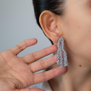 May include: A pair of long, dangling earrings made of silver beads. The beads are arranged in a cascading pattern, creating a delicate and elegant look.