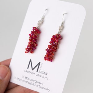 May include: A pair of red beaded dangle earrings with silver hooks. The earrings are displayed on a white card with the text "ML CROCHET JEWELRY" and a website address.