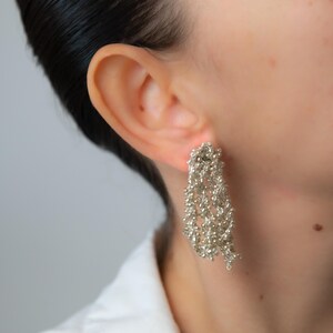 May include: Silver-toned dangle earrings with a textured, clustered design. The earrings are worn on a person's ear, showcasing their intricate, cascading appearance. The earrings are a statement piece.