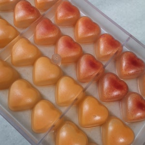 May include: A clear plastic mold filled with heart-shaped candies. The candies are a gradient of orange and red.