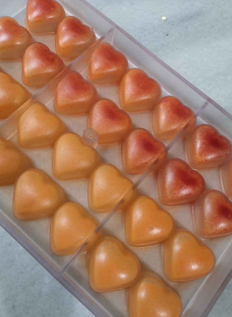 May include: A clear plastic mold filled with heart-shaped candies. The candies are a gradient of orange and red.