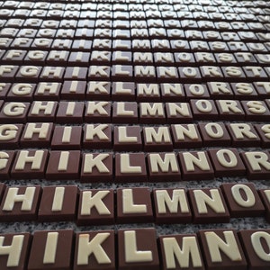 May include: A close-up of a collection of chocolate letters, arranged in rows, with the letters A through Z. The letters are made of dark chocolate and have white lettering.