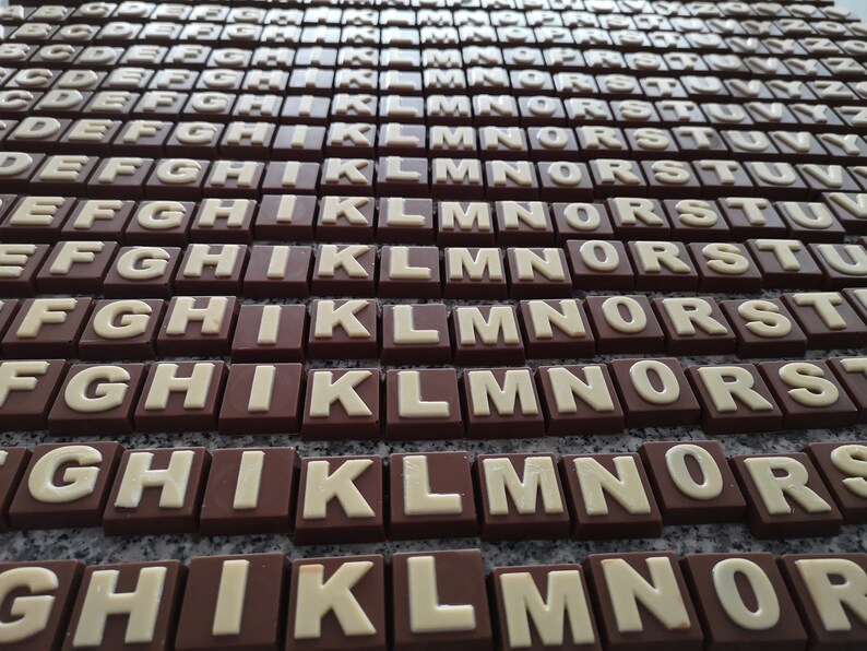 May include: A close-up of a collection of chocolate letters, arranged in rows, with the letters A through Z. The letters are made of dark chocolate and have white lettering.