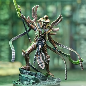 Può includere: Una miniatura dettagliata di una figura scheletrica con vernice dorata metallica e verde, che tiene una lama verde e indossa un copricapo piumato. La figura è in posa dinamica, con le braccia distese e le gambe piegate. La miniatura è posizionata su una base verde e marrone.
