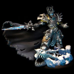 May include: A detailed figurine of a skeletal warrior in dark armour, holding a glowing blue sword. The figure stands on a snowy base with a skull, wearing a black cape and a crown. The overall colour scheme is dark with blue and gold accents.