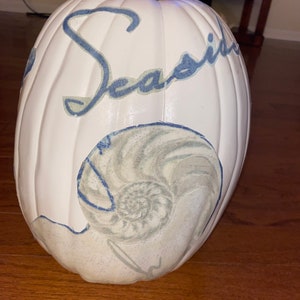 May include: White pumpkin with blue lettering that says "Seasid" and a blue and grey seashell design.
