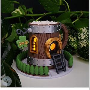 May include: A miniature wooden pub shaped like a beer mug with a green shamrock sign that says "pub". The pub has a small window and a door with a horseshoe above it. There are green bushes around the base of the pub.