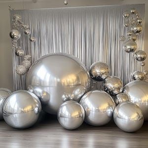 May include: A collection of shiny silver spheres of varying sizes, arranged in front of a silver, textured backdrop. The spheres reflect light, creating a bright and festive display. The arrangement suggests a decorative or celebratory theme.