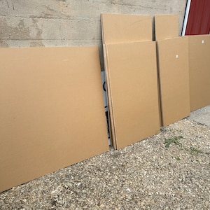 May include: A stack of six brown cardboard sheets leaning against a concrete wall. The sheets are various sizes and are stacked in a staggered pattern.