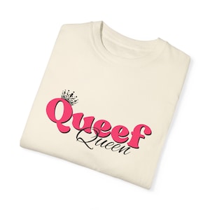 May include: A white t-shirt with a pink graphic that says "Queef Queen" with a crown above the word "Queef".