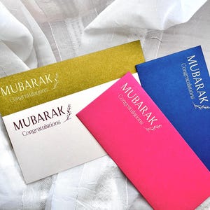 May include: Three envelopes with the word "MUBARAK" and "Congratulations" printed on them. The envelopes are gold, pink, and blue.