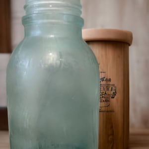 May include: A frosted glass bottle with a textured surface. The bottle is clear and has a light blue tint. The bottle is sitting next to a wooden container.
