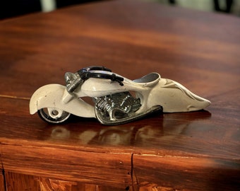 May include: White toy motorcycle with black handlebars and a silver engine. The motorcycle has a white and silver paint job with a black stripe on the side.