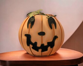 May include: A smiling orange pumpkin with a black face and a green stem. The pumpkin is sitting on a wooden table.