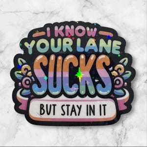 May include: A black sticker with the text "I KNOW YOUR LANE SUCKS BUT STAY IN IT" in colorful bubble letters. The sticker has a decorative floral design and holographic accents.