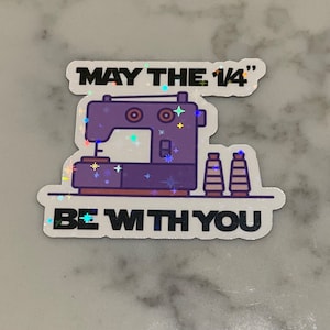 May include: A white sticker with a sewing machine and spools of thread. The text on the sticker reads "May the 1/4" be with you".