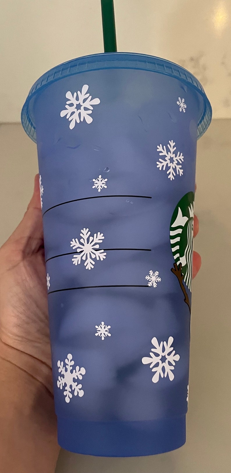 Puede incluir: Un vaso fr&iacute;o de pl&aacute;stico azul de Starbucks con tapa a juego y pajita verde. La taza est&aacute; decorada con copos de nieve blancos. El logotipo de Starbucks es visible en el lateral.