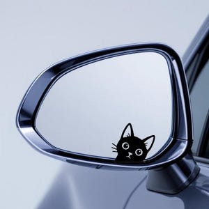 Puede incluir: Una pegatina de gato negro en el espejo lateral de un coche. El gato tiene ojos grandes y una expresi&oacute;n de sorpresa. El espejo es cromado y refleja el cielo. El coche es de color azul claro.