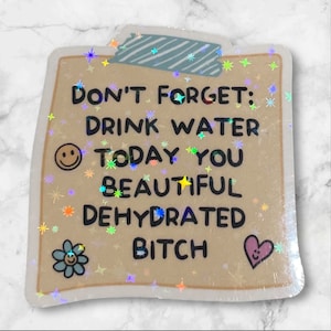 May include: A holographic sticker with a light brown background and a white border. The sticker has a message that reads "Don't forget: Drink water today you beautiful dehydrated bitch". The sticker has a smiley face, a flower, and a heart with a smiley face.