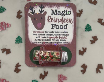 May include: A festive card with the words "Magic Reindeer Food" and a reindeer illustration. A small glass vial filled with colorful sprinkles is attached. The card includes instructions for use. Christmas-themed confetti surrounds the card.