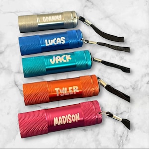 May include: Five colorful mini flashlights with personalized names: Grammy, Lucas, Jack, Tyler, and Madison. Each flashlight has a black lanyard.