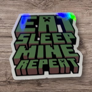 May include: A white sticker with a green and brown Minecraft-themed design. The sticker says "Eat Sleep Mine Repeat" with a creeper face at the beginning and end of the text.