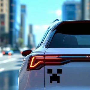 May include: White car with a black pixelated face decal on the rear. The car's taillight is illuminated with a bright orange glow. The background shows a blurred city street with buildings and a blue sky.