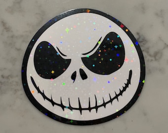 Op de afbeelding: Een ronde sticker met een zwarte rand en een witte achtergrond. De sticker heeft een zwart-witte illustratie van Jack Skellingtons gezicht uit de film The Nightmare Before Christmas. Het gezicht is bedekt met iriserende glitter.
