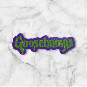 May include: A die-cut sticker featuring the word Goosebumps in a stylized, jagged green font with a dark purple outline. The lettering is decorated with small, colorful, multi-pointed star shapes in shades of blue, pink, yellow, and orange.