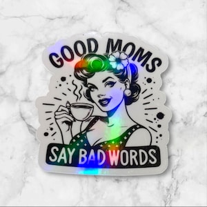 May include: Holographic sticker featuring a retro-style illustration of a woman holding a coffee cup. The sticker reads "GOOD MOMS SAY BAD WORDS" in black text. The woman has dark hair and is wearing a dress.