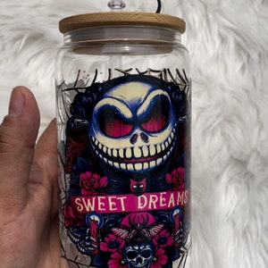 May include: A clear glass tumbler with a bamboo lid and a black and white Jack Skellington character design. The tumbler has a straw with a black and white Jack Skellington character topper. The design includes the words "Sweet Dreams" and a skull with flowers.
