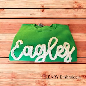 May include: Green sweatshirt with white fluffy embroidered lettering that says "Eagles".